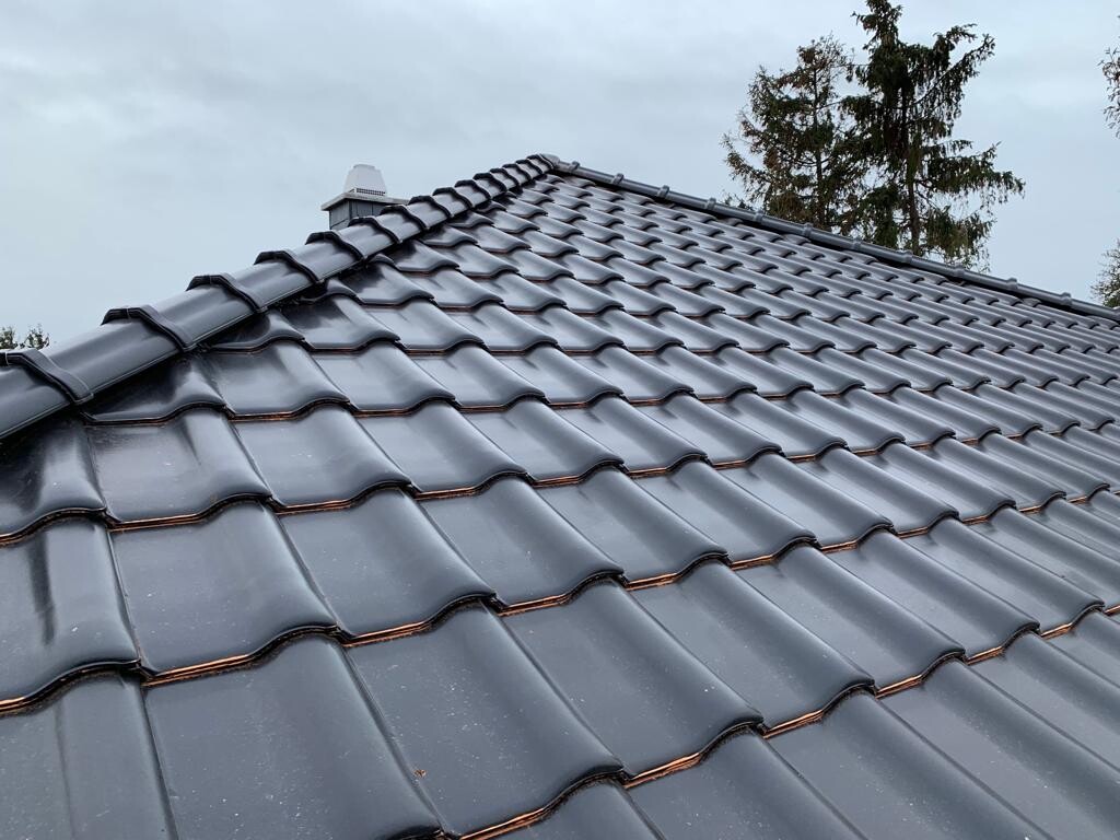 Dach mit grauen, gewellten Ziegeln; Blick über geneigte Dachfläche, Wolkenhimmel.