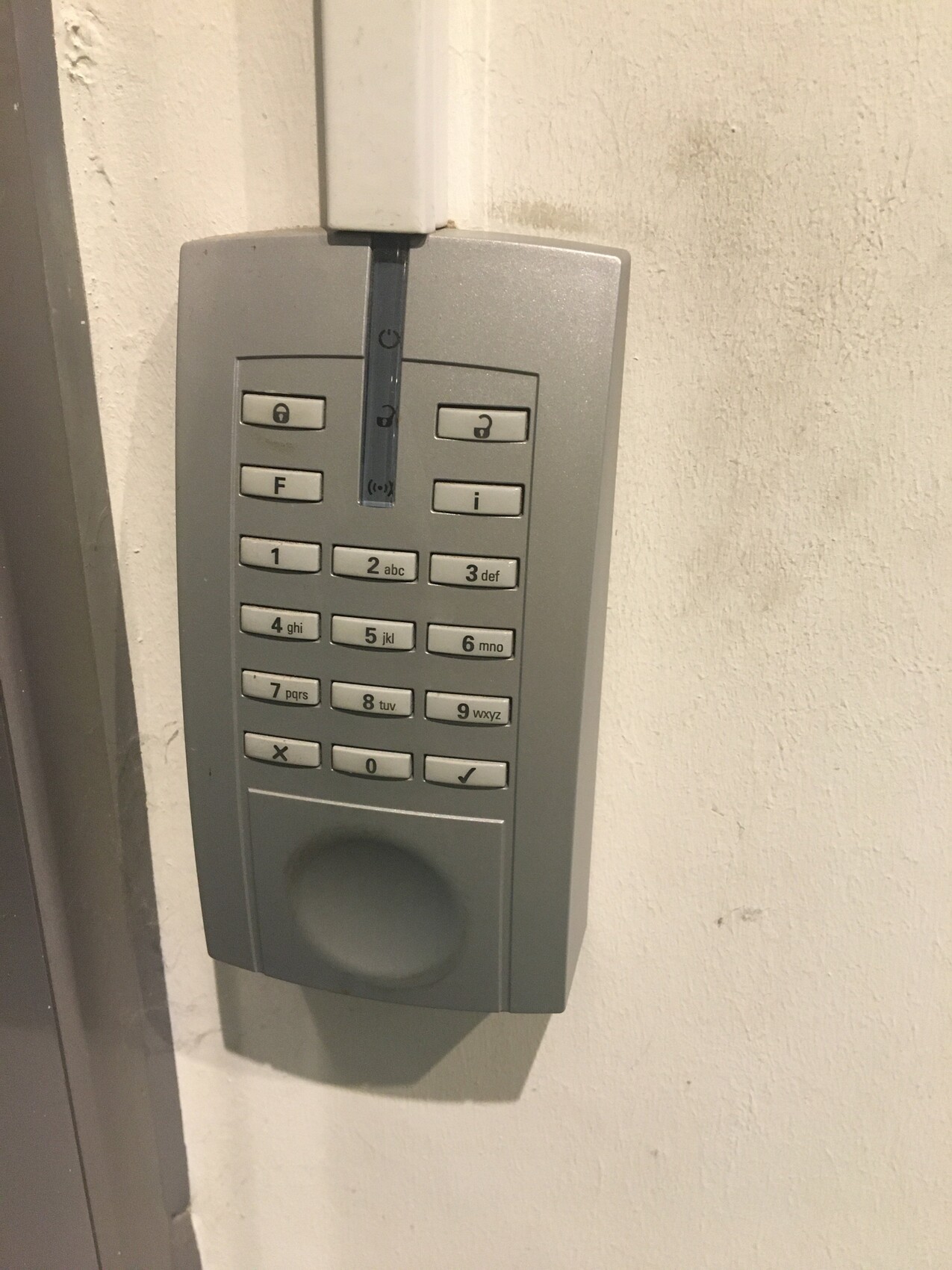 Graues Tür-Zugangstastfeld mit Ziffernblock an weißer Wand.