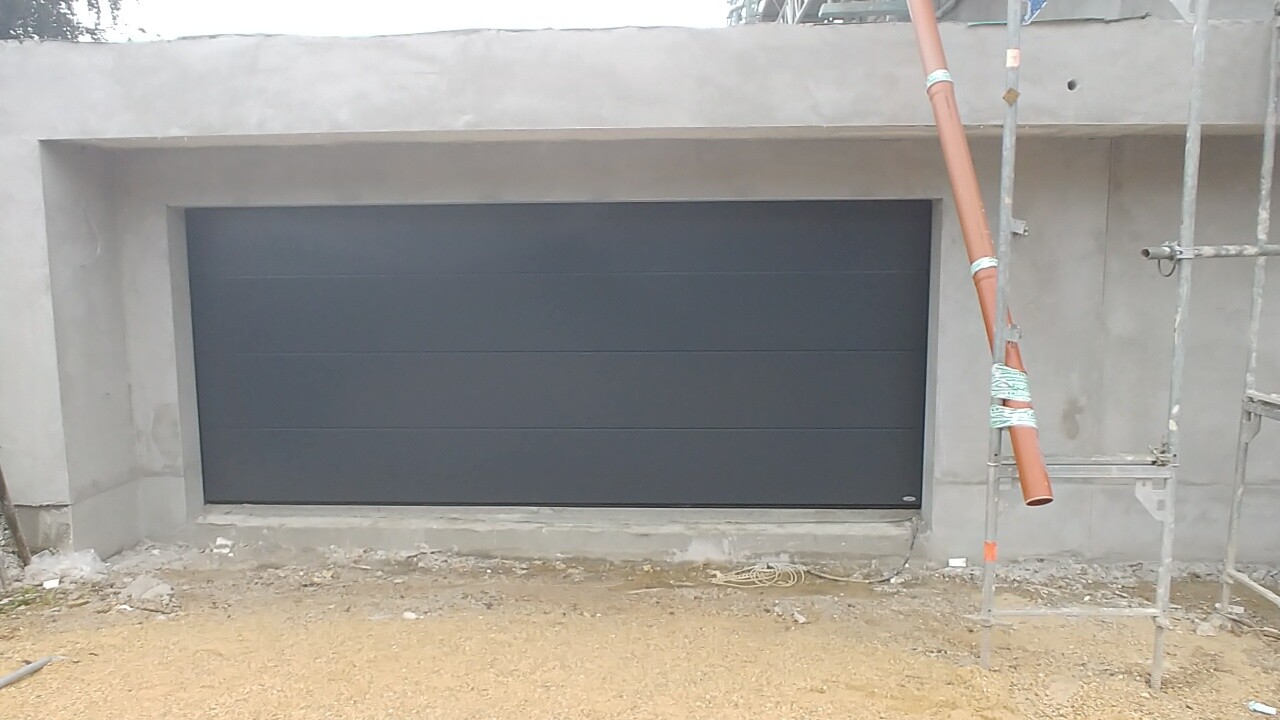 Graues Garagentor vor roher Betonfassade mit Baugerüst