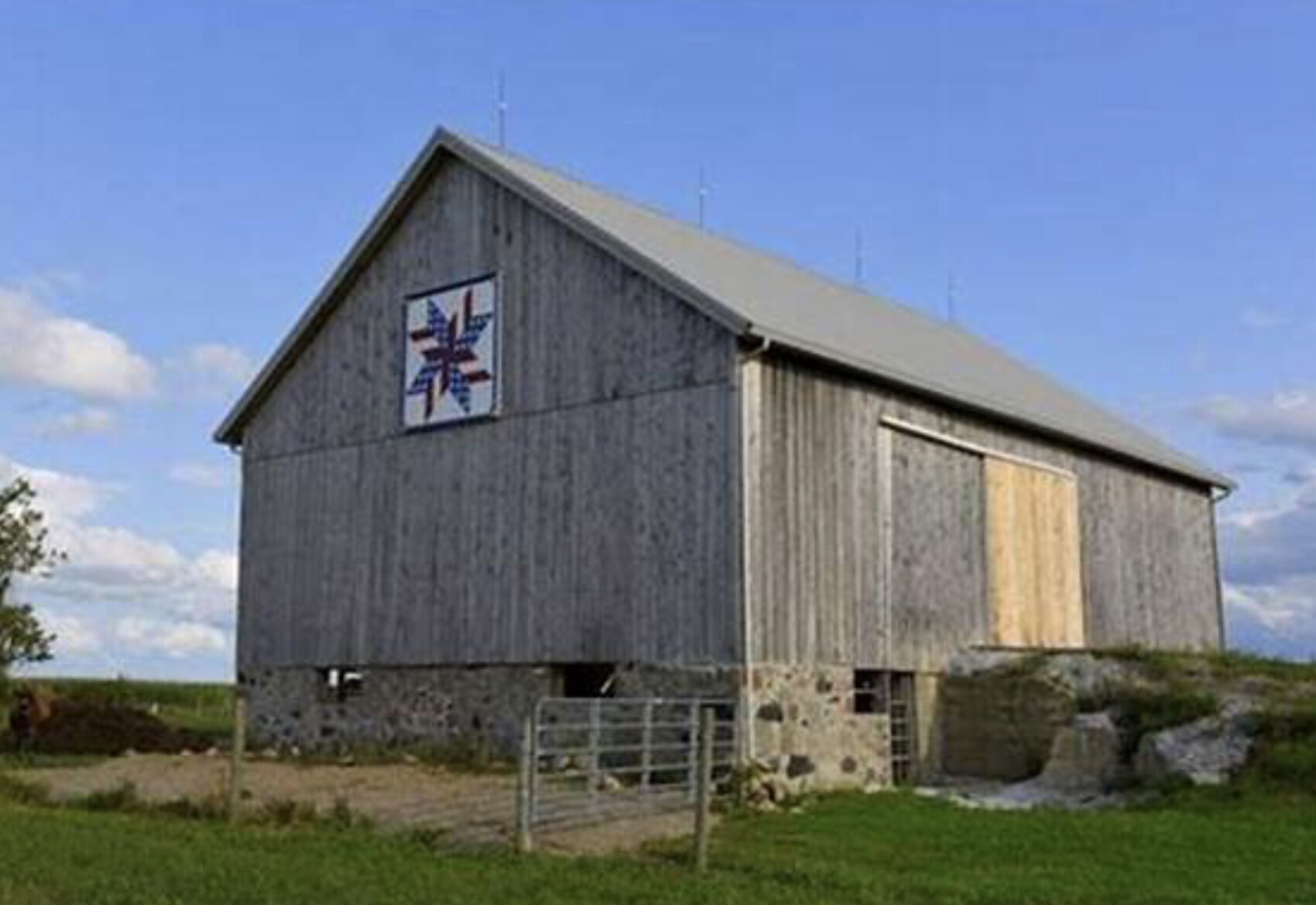 Grau holzverkleidete Scheune auf Steinfundament mit Torfront und blauem Himmel.