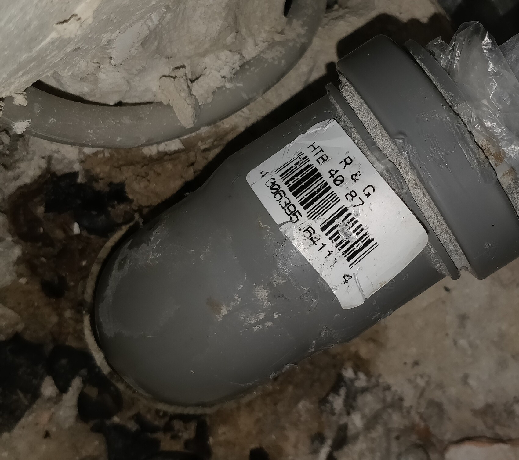 Grau PVC-Abflussrohrbogen mit Barcode-Etikett in staubiger Umgebung