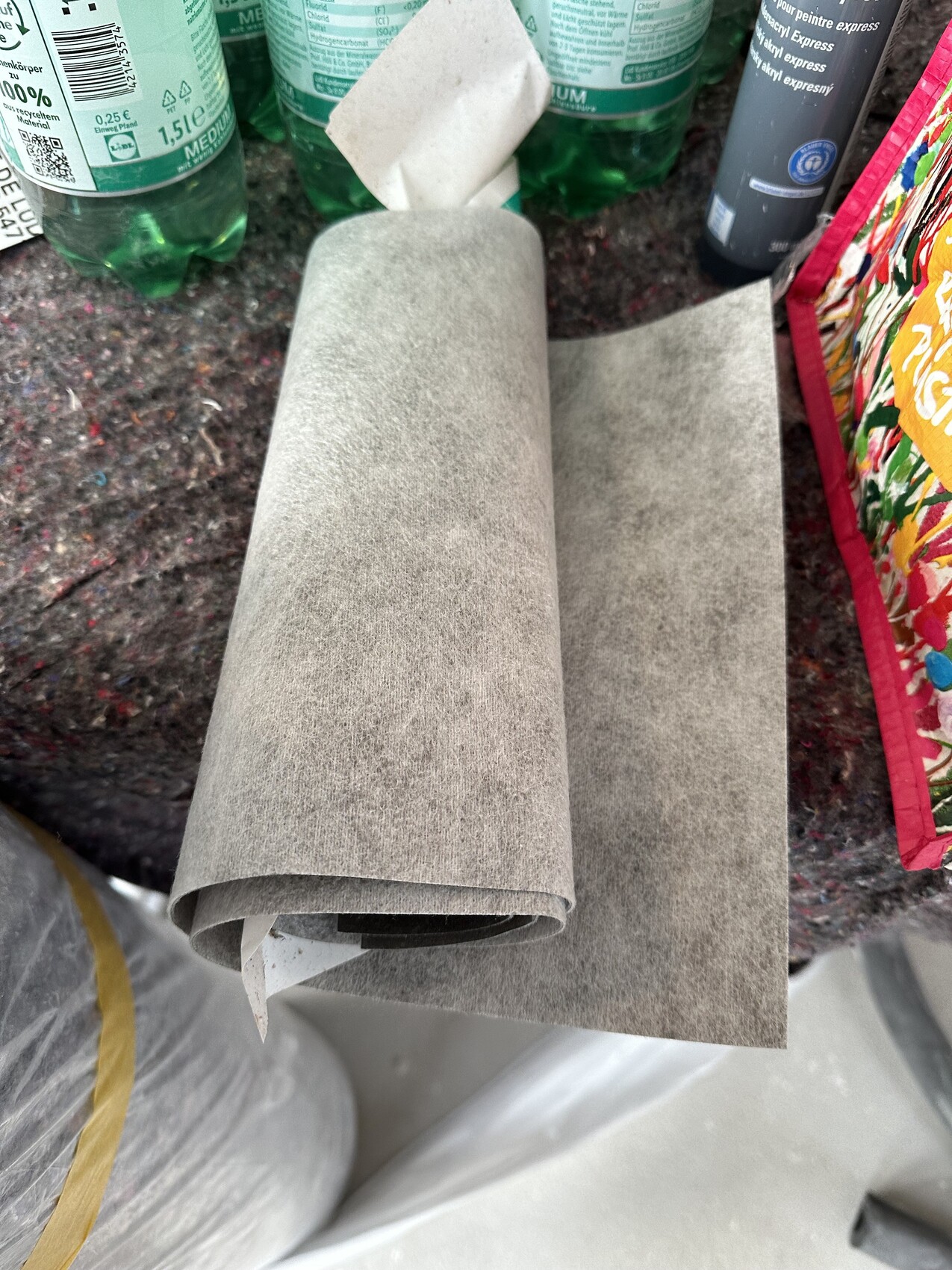 Graue Schleifpapierrolle liegt auf einer Werkbank neben Farben und Putzmaterialien.