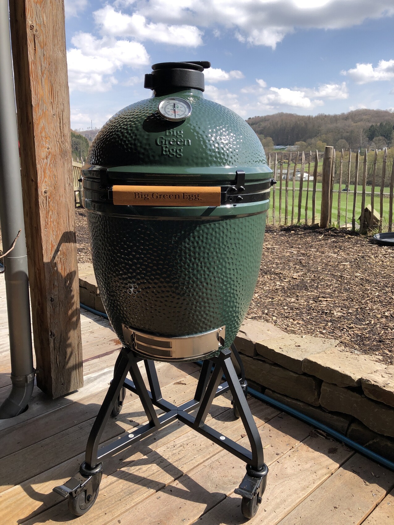 Grüner Big Green Egg Keramik-Grill auf Gestell im Freien, mit Thermometer.