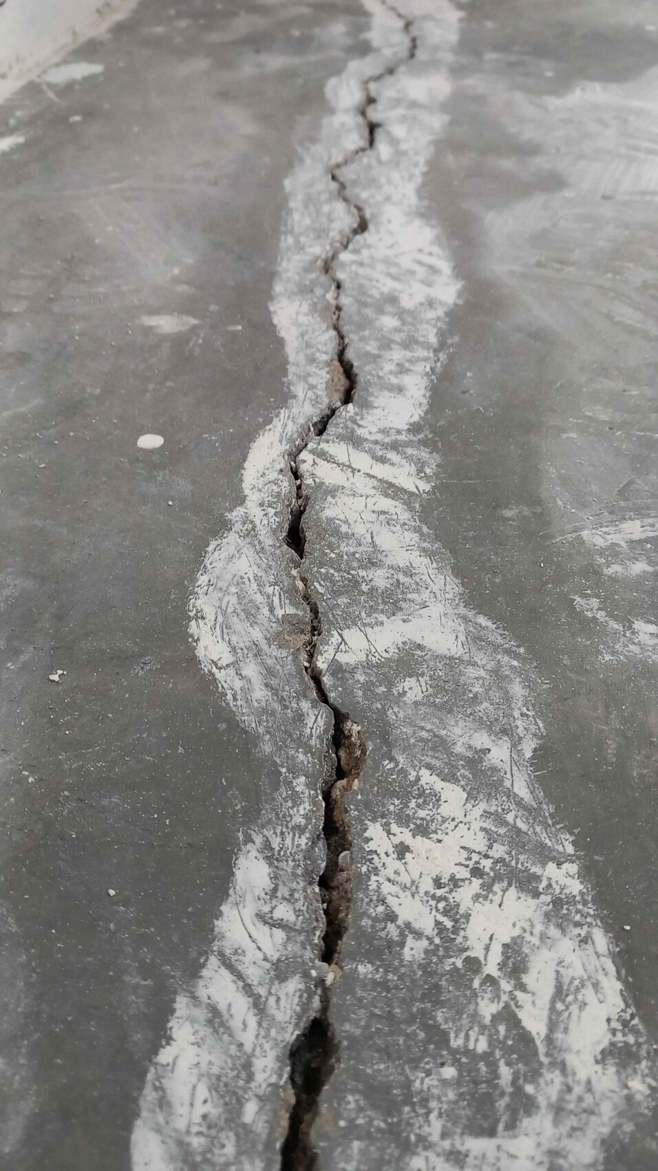 Rissiger Betonboden mit einer langen vertikalen Spalte und weißem Staub