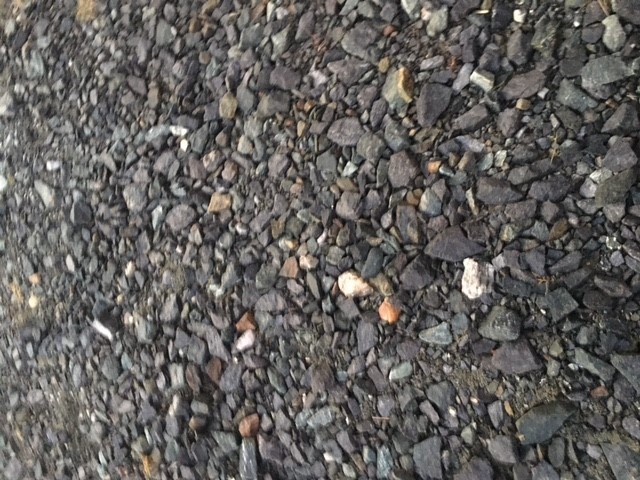 Graue und dunkle Kiesel auf rauem Kies- oder Asphaltbelag.
