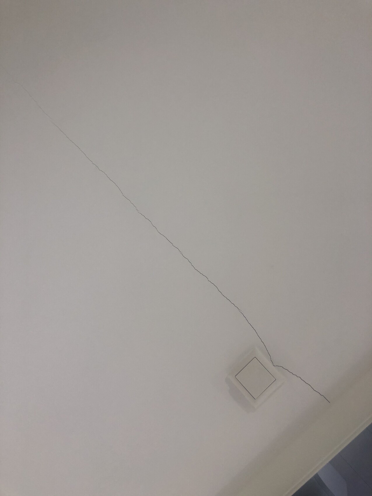 Weiße Decke mit diagonaler Risslinie, nahe einer quadratischen Deckenleuchte.