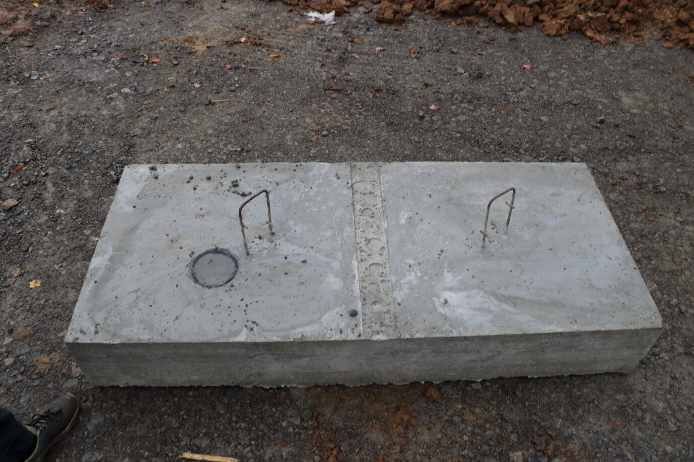 Betonplatte auf Baustellengrund mit zwei Metallbügeln an den Enden.