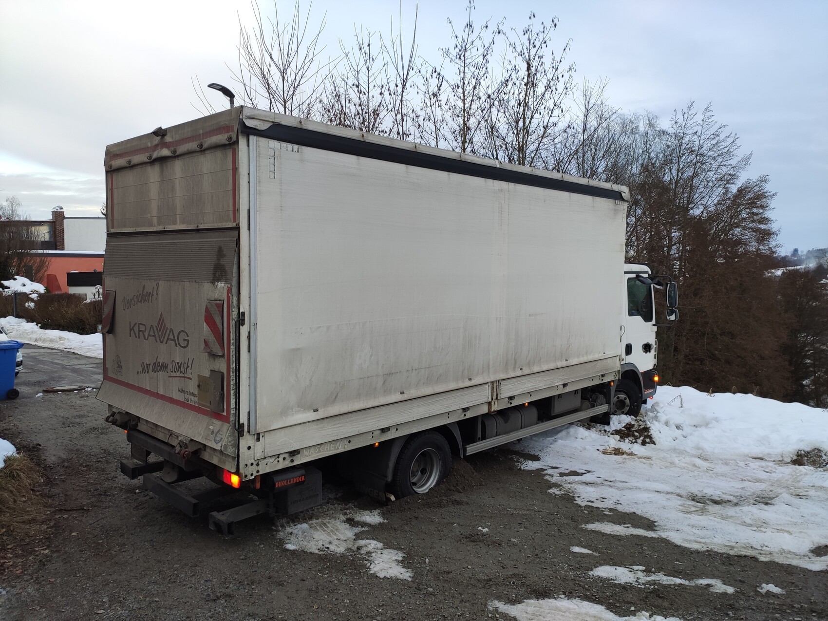 Großer weißer LKW mit Box-Aufbau steht im Schnee; Wald im Hintergrund.
