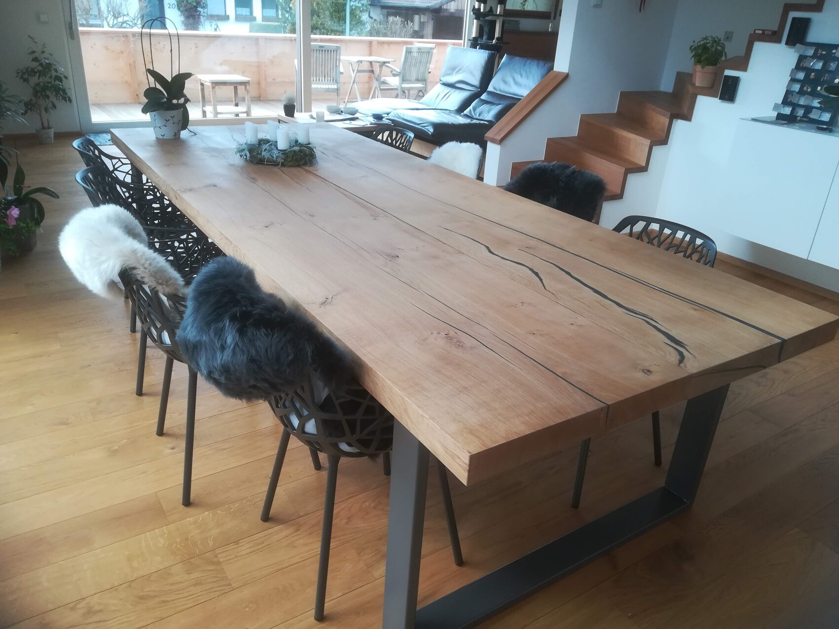 Großer Holztisch mit Maserung und Metallgestell im offenen Wohnzimmer; Stühle mit Fellauflagen.
