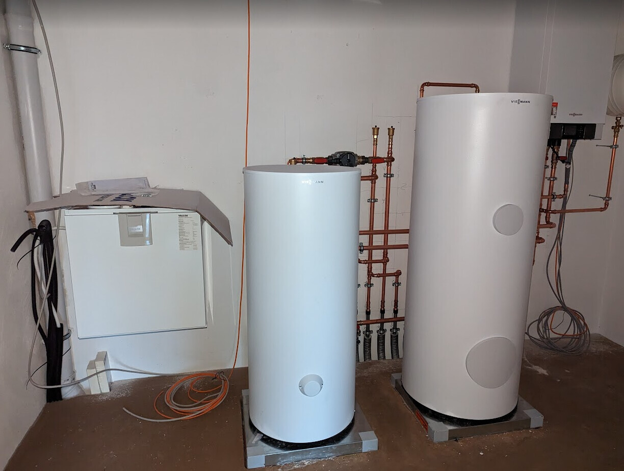 Keller mit zwei weißen Viessmann-Warmwasserboilern, sichtbare Kupferrohre und Installationen.