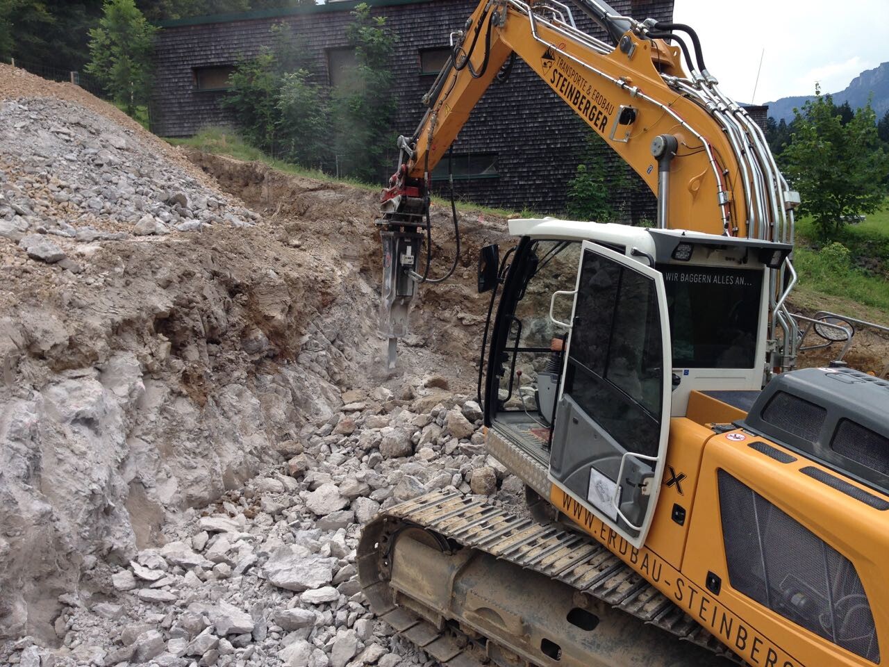 Große gelbe Baumaschine baggert auf einer Baustelle neben einem Geröllhügel