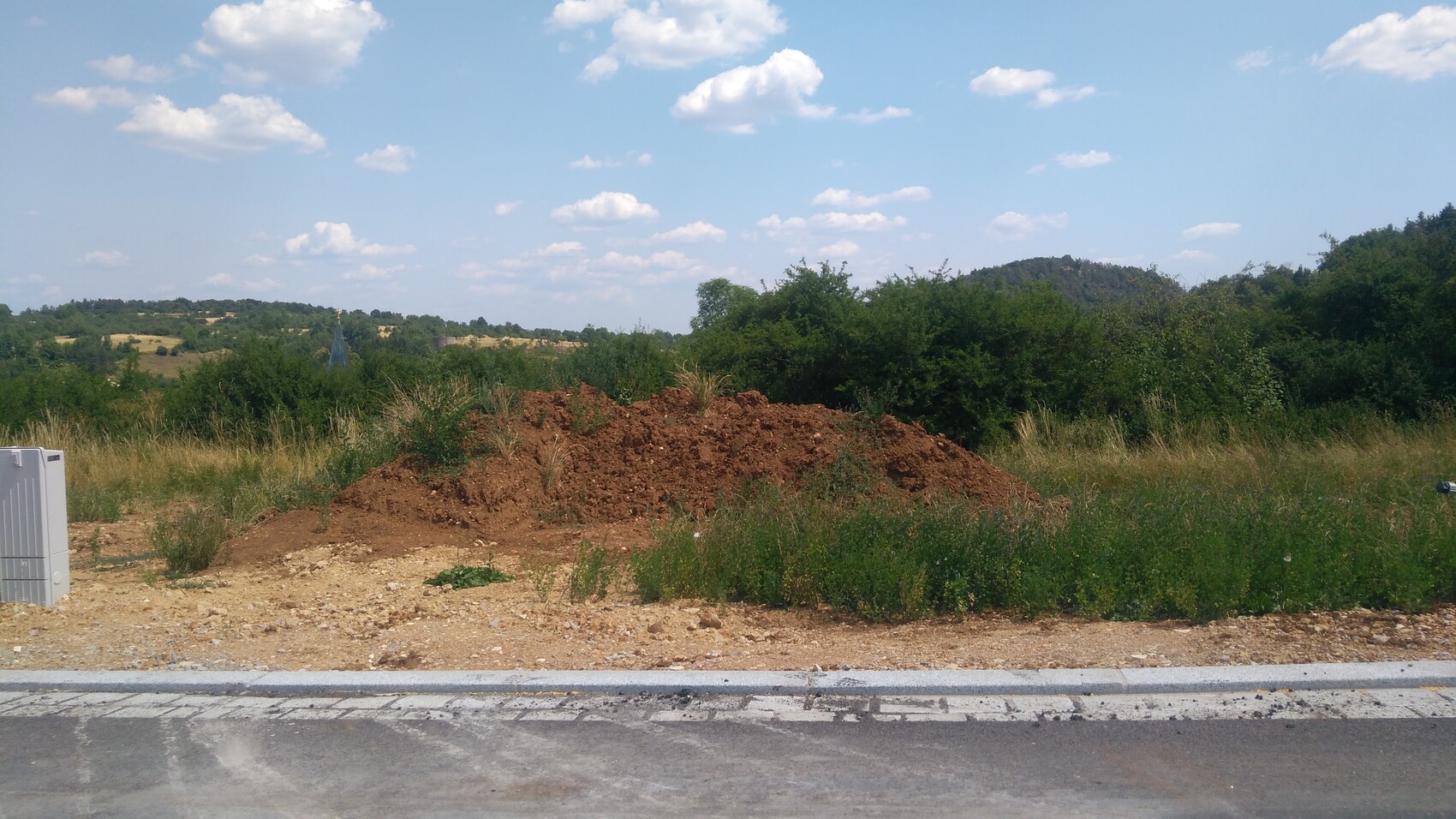 Großer Erdaushub-Hügel am Straßenrand in ländlicher Landschaft mit Büschen und Himmel