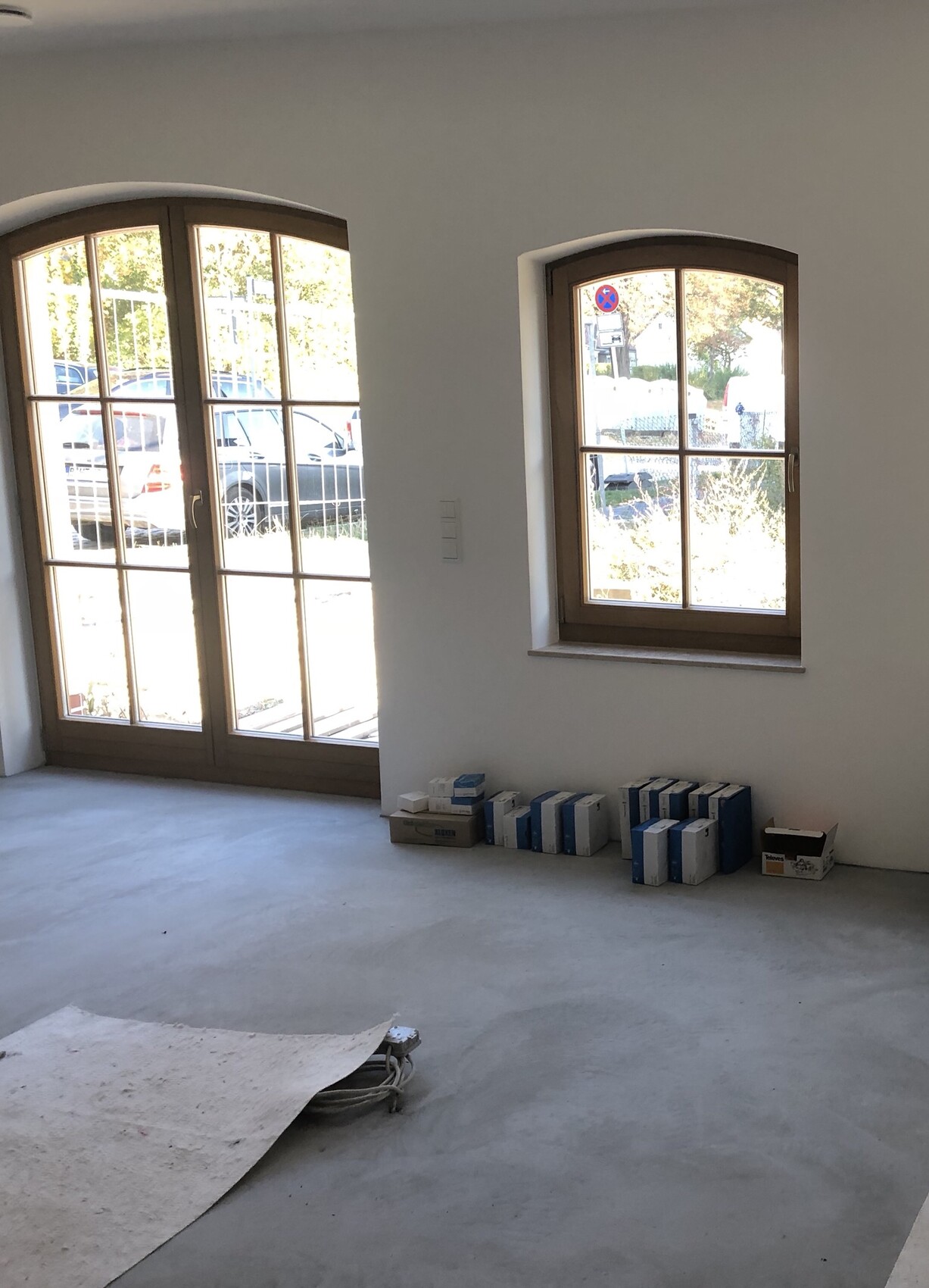 Unfertiger Innenraum mit großen Bogentüren, Fenster und Baumaterialien am Boden.