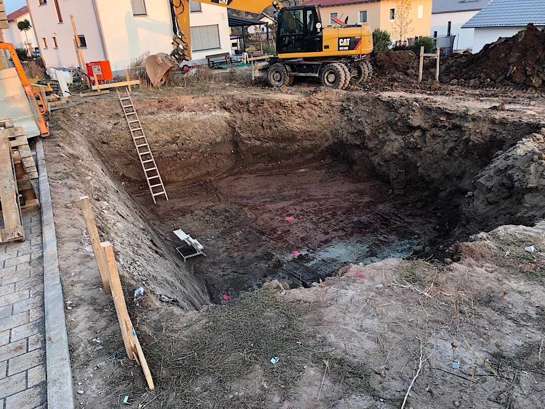 Grosse Baugrube mit Bagger auf Wohnbaustelle, Fundamentarbeiten sichtbar