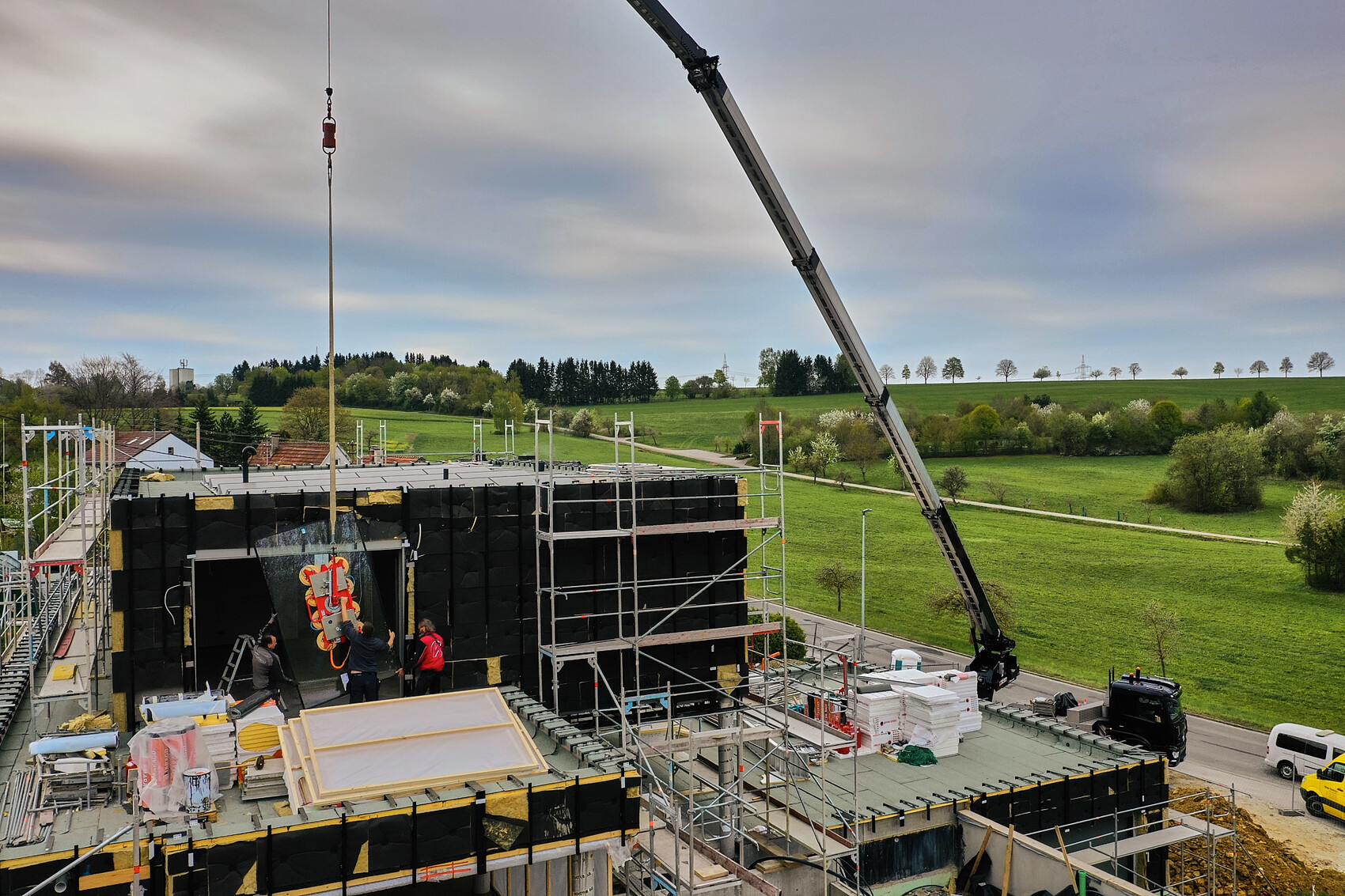 Baustelle mit Kran, Geruest und Bauarbeitern am Rohbau auf gruenem Land.