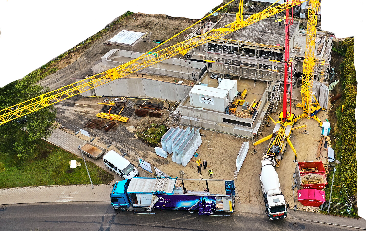 Vogelperspektive: Baustelle mit gelbem Kran, Gerüst, Bauarbeiten, LKWs und Betonplatten.