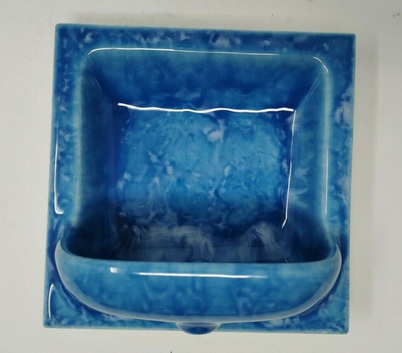 Große blaue Badewanne in quadratischem Becken mit glänzender Oberfläche