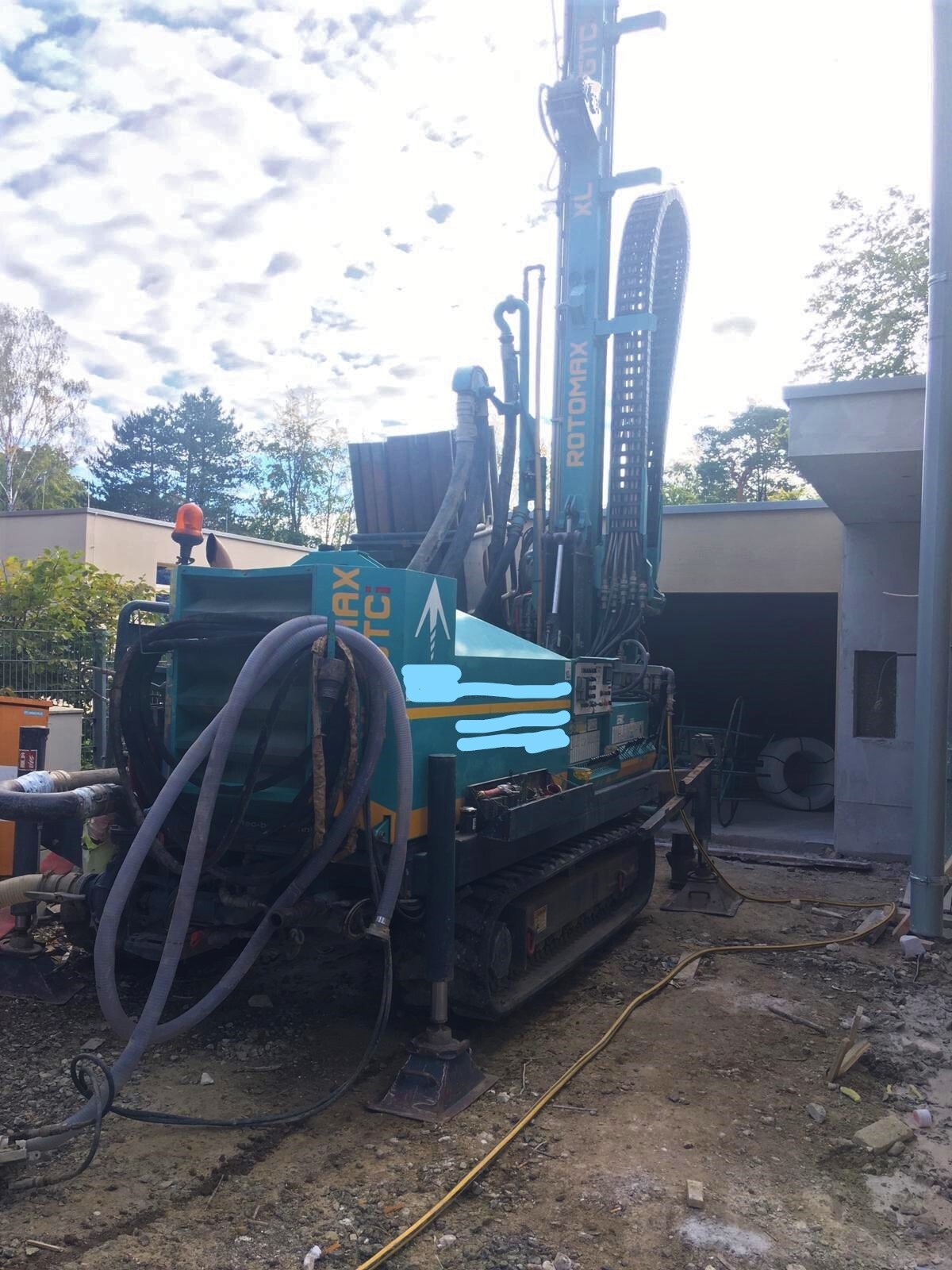 Blaue Kettenbohranlage mit Hydraulikschläuchen auf einer Baustelle.