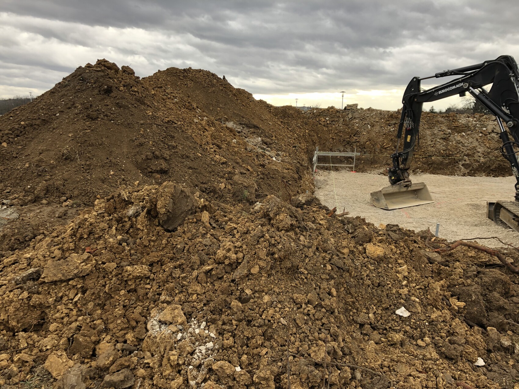 Große Erdhaufen und ein Bagger auf einer Baustelle bei Erdarbeiten