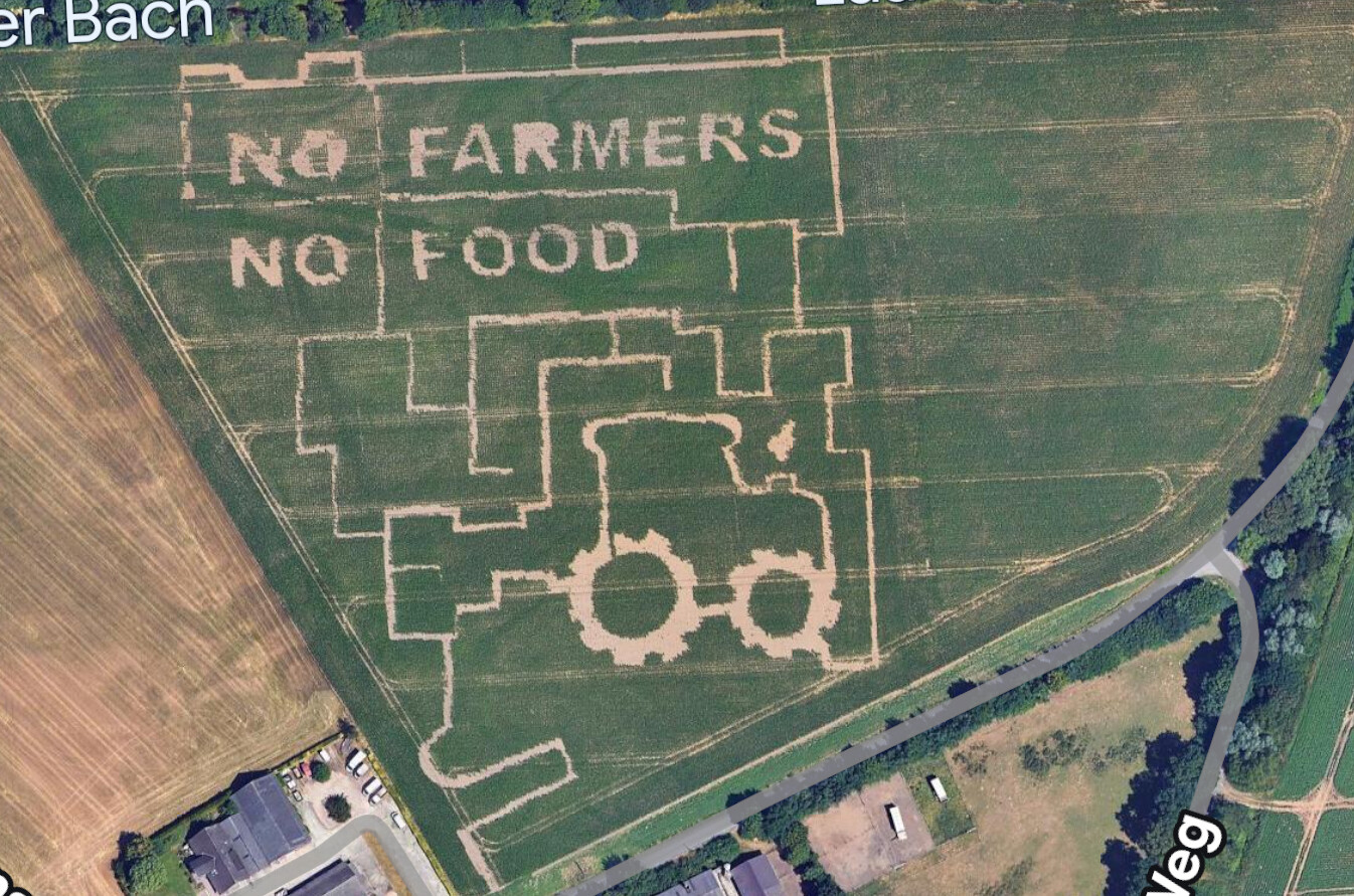 Luftbild eines Getreidefelds mit der Botschaft 'NO FARMERS NO FOOD' und Traktoren-Silhouette.
