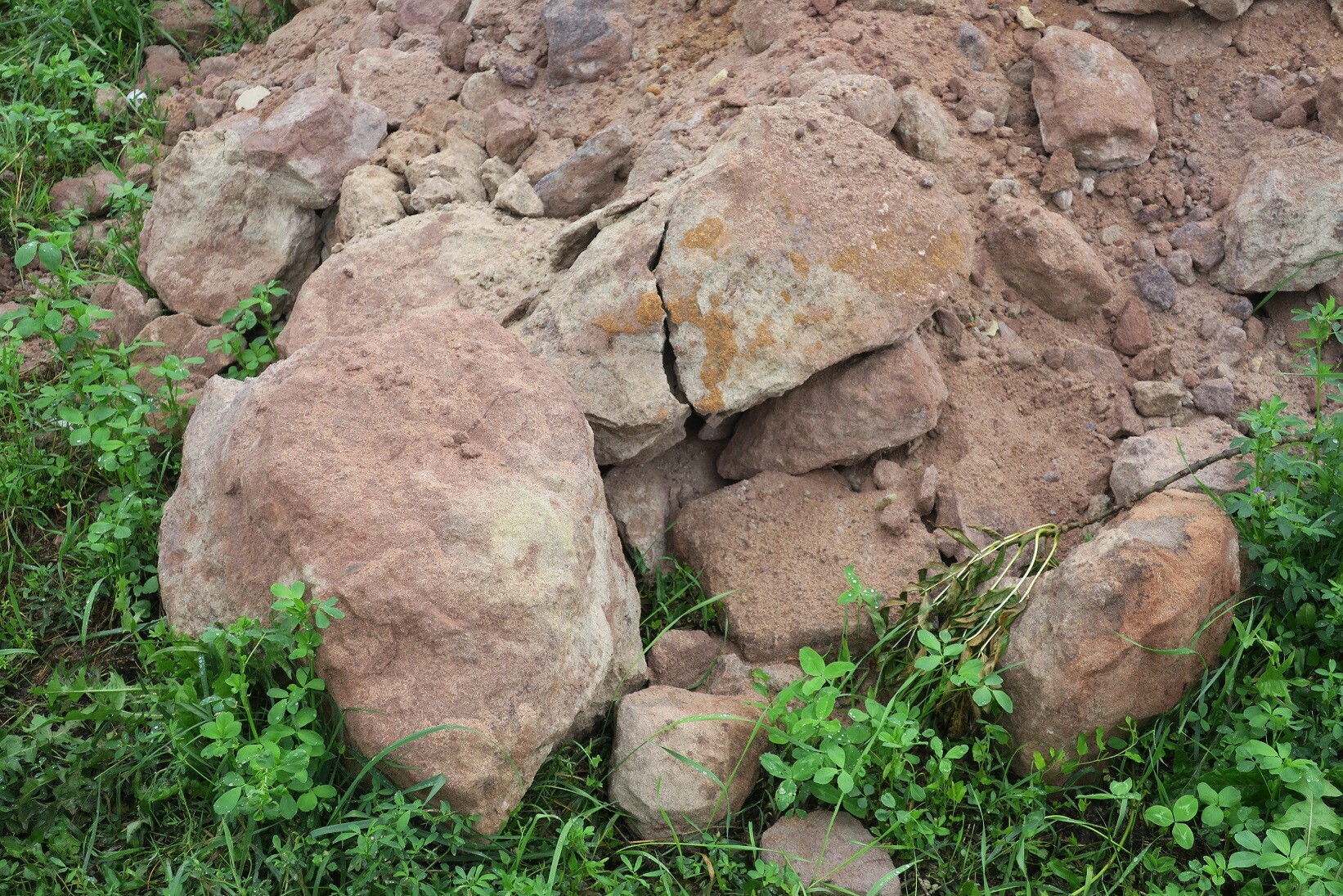 Unordnung aus großen Felsbrocken auf Baugrund mit Gras und Unkraut