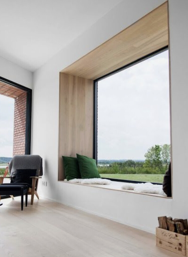Große Fensterbank mit Holzeinfassung, grüne Kissen, Blick ins Grüne, heller Wohnraum.