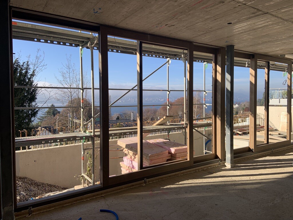Unfertiges Bauprojekt: Große Fensterfront, Gerüst außen, Dämmplatten, Blick auf See.