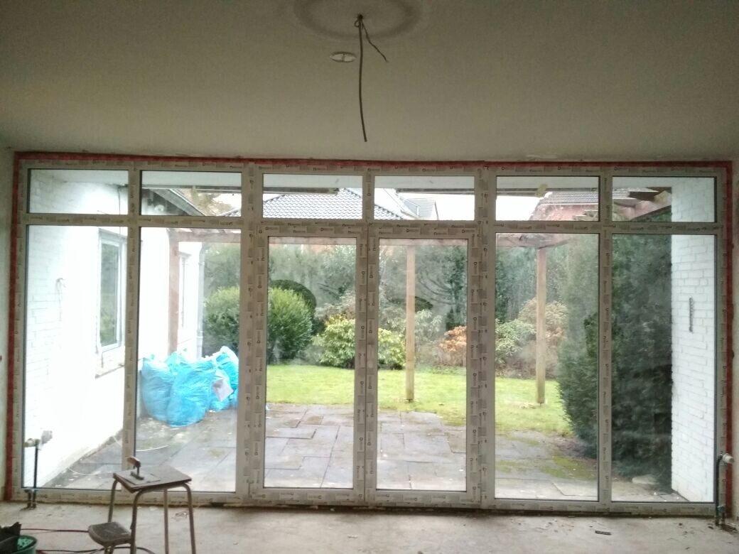 Große Glas-Schiebetürenfront zum Garten; Innenraum unfertig, Garten mit Rasen, Bäumen und Sträuchern