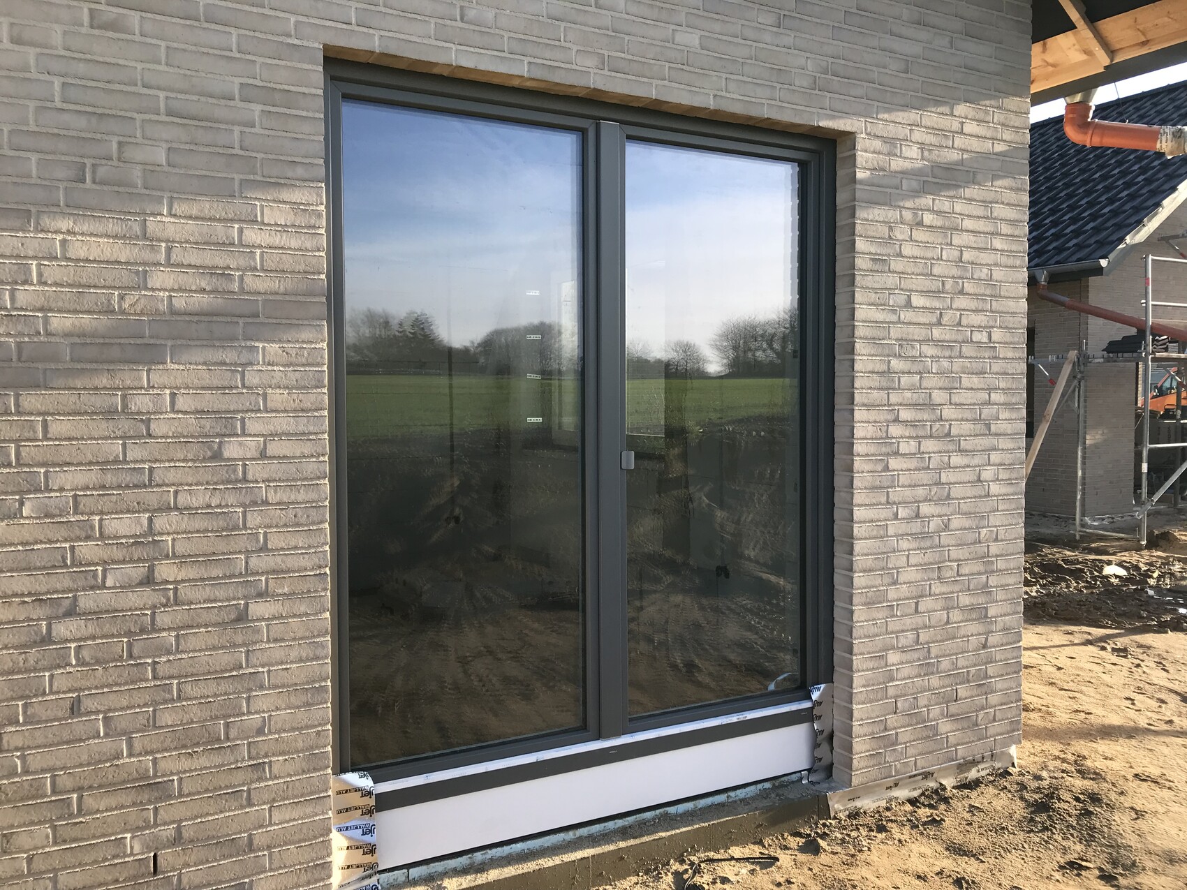 Großes Glas-Schiebetürfenster in einer Ziegelwand; Baustelle mit Gerüst und Erde.