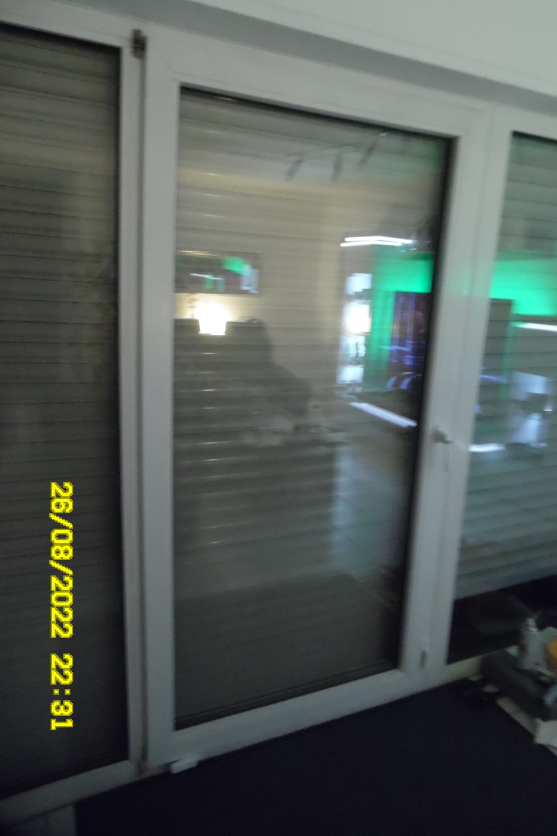 Glasfront mit weißem Rahmen; Innenraum mit grünem Neonlicht und Reflexionen.