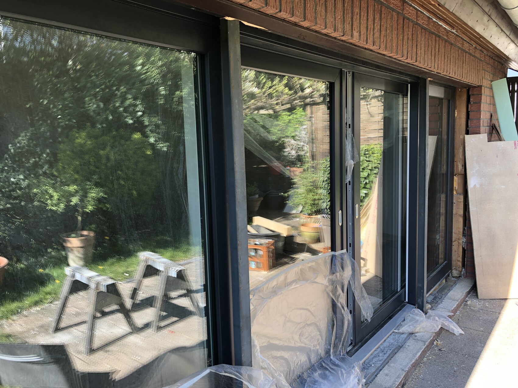 Glas-Schiebetüren bei Renovierung; Schutzfolie am Rahmen, Bauwerk im Garten, Leitern daneben
