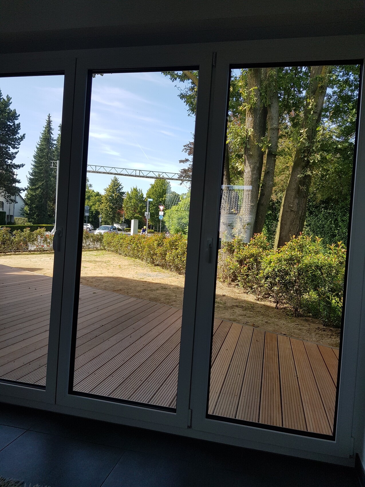 Blick durch große Glassfronten auf Terrasse, Garten und Bäume