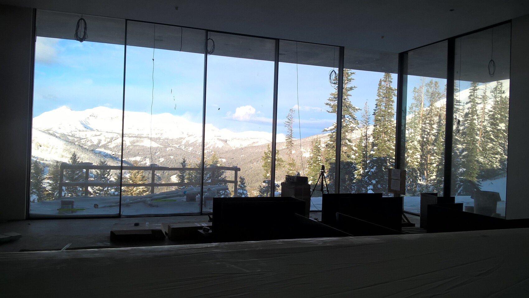 Innenraum mit Glasfenstern, Blick auf verschneite Berge und Wald; Ausrüstung im Vordergrund.