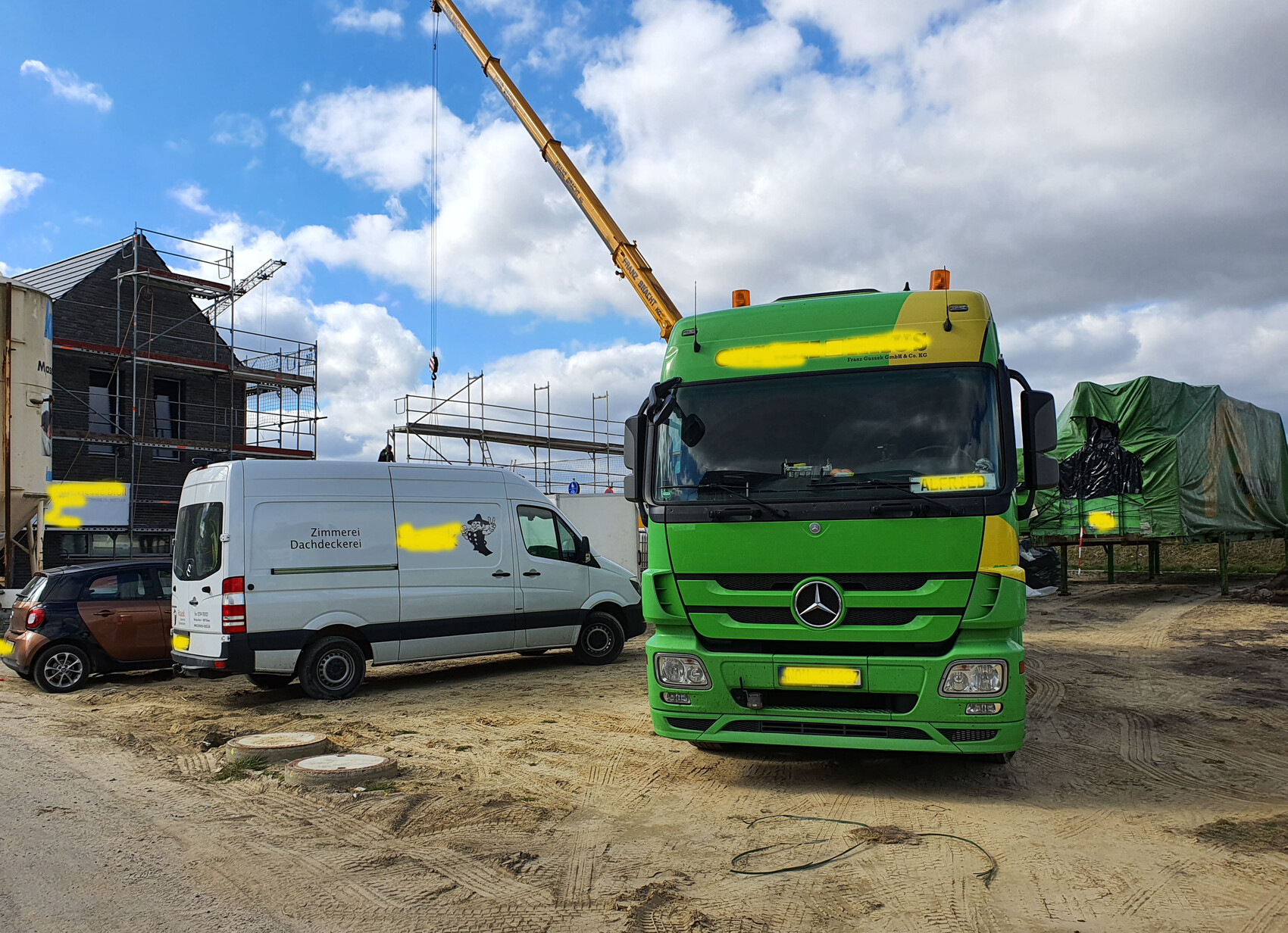 Baustelle mit grünem Mercedes-LKW, weißem Lieferwagen, Gerüsten und Baukran vor unfertigem Haus.
