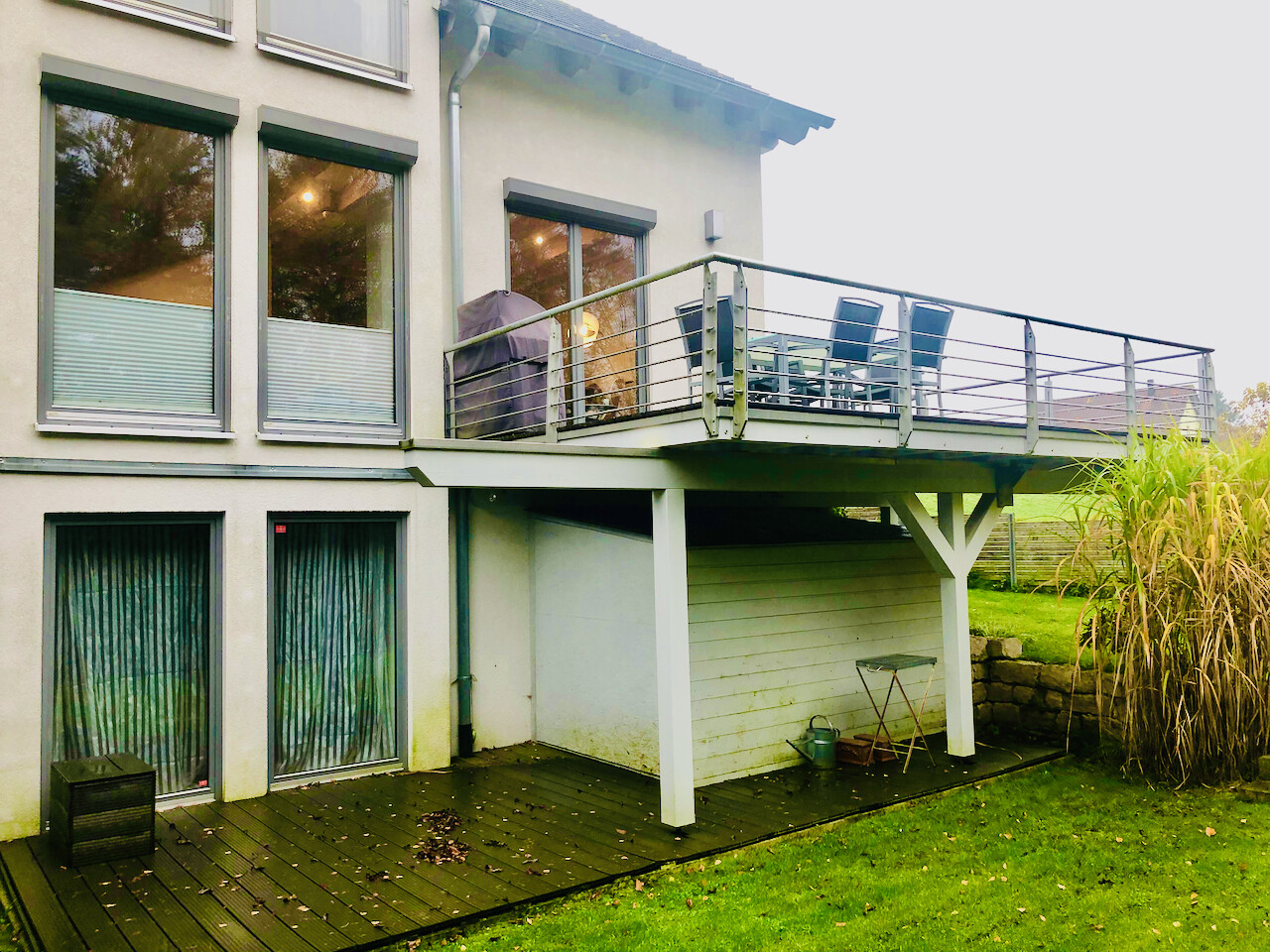 Zweistöckiges Haus mit Oberdeck-Terrasse, Geländer, Grill, Stühlen und Garten
