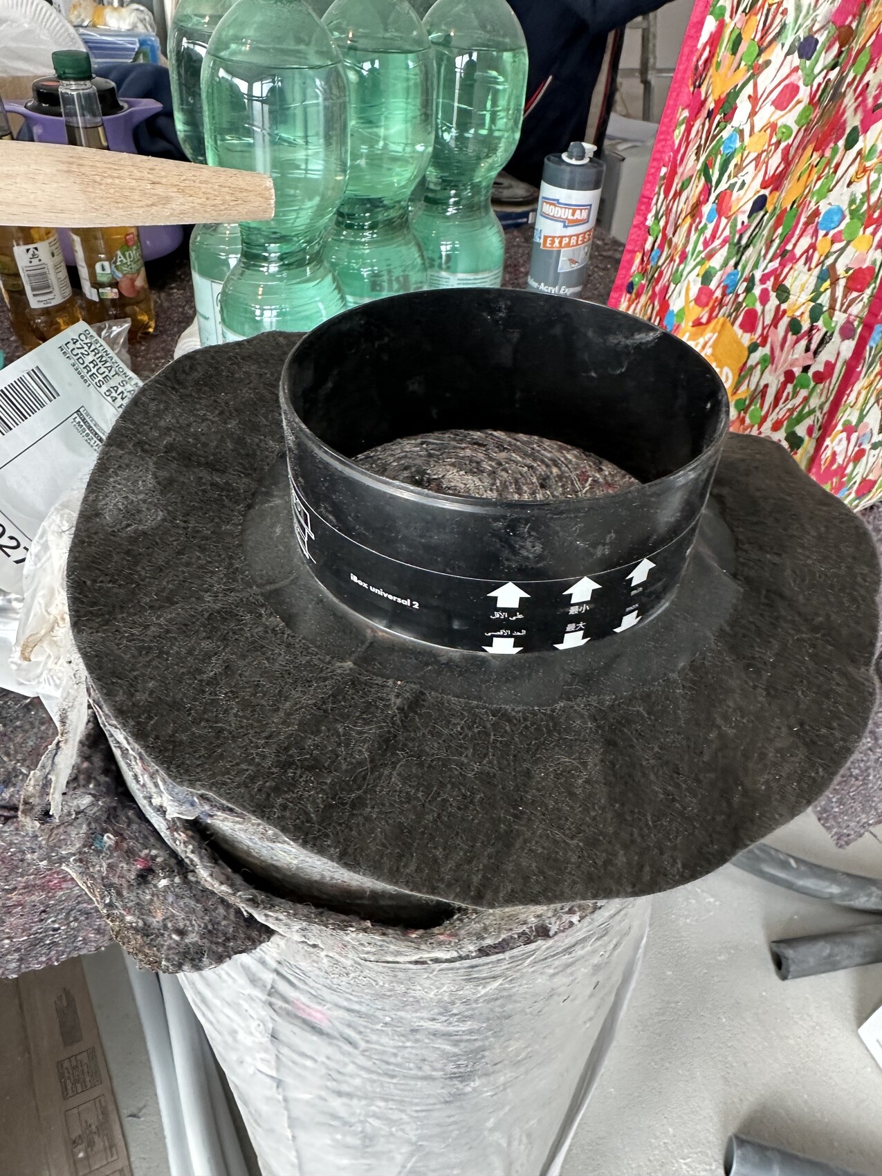 Großer schwarzer runder Lüftungskanal in Werkstatt, umgeben von Farben und Materialien.