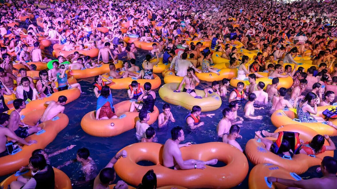 Viele Menschen in überfülltem Pool mit bunten orangefarbenen und gelben Aufblasringe.