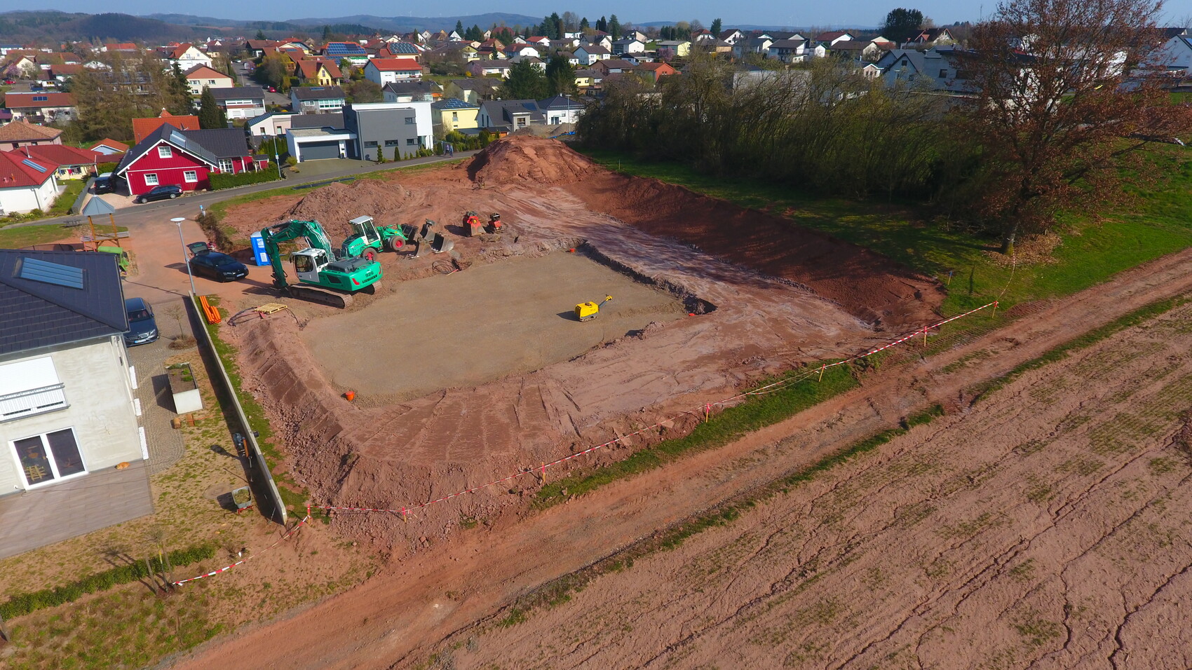 Baugrundstück im Wohngebiet mit Baumaschinen, Erdaushub und Absperrband.