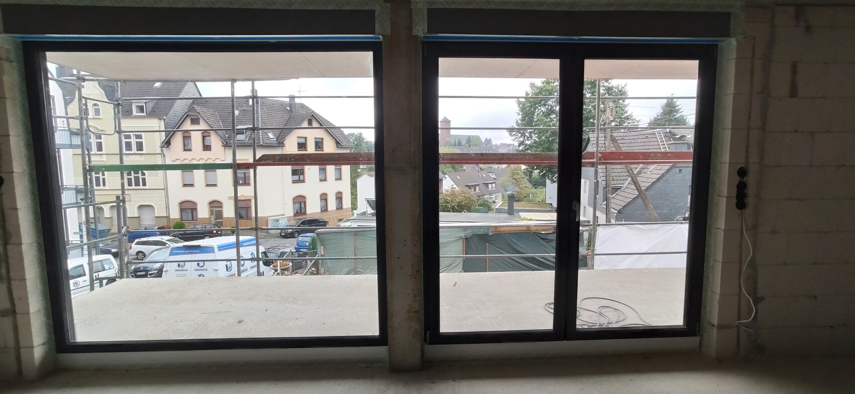 Unfertiger Innenraum mit großen Fenstern, Blick auf Baugerüste und Häuserstraße.