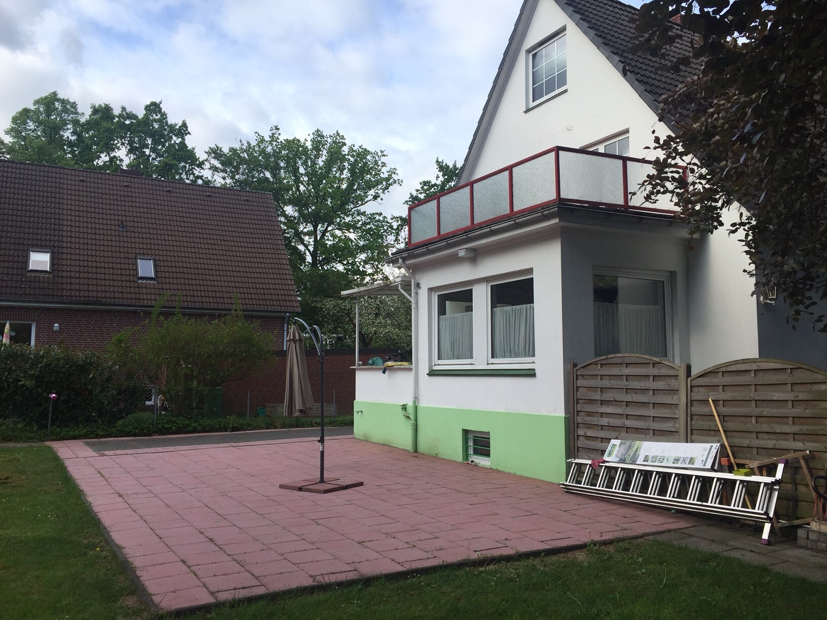 Garten hinter weißem Haus mit grünem Sockel, pinke Terrasse, Balkon mit rotem Geländer, Leiter.