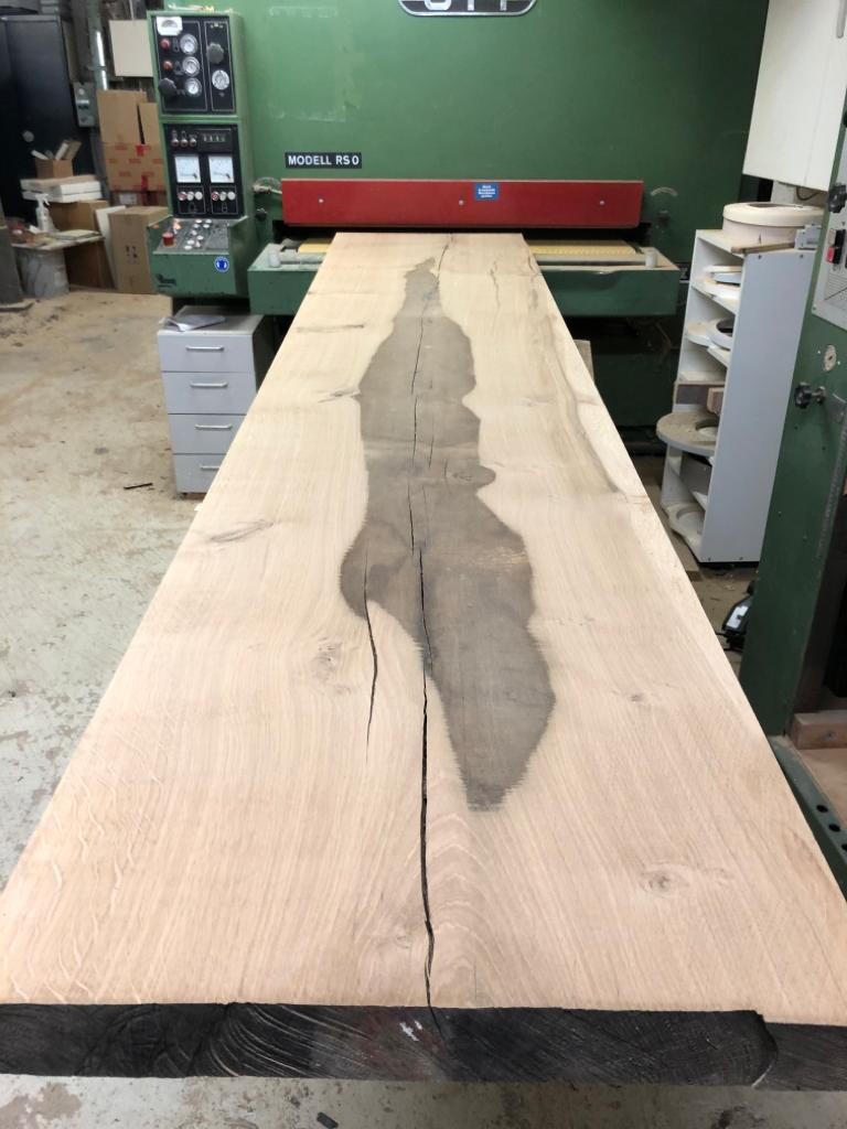 Großes Holzbrett mit zentralem Riss und dunkler Verfärbung in einer Holzwerkstatt.