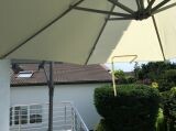 Terrasse mit Sonnenschirm, Geländer und Blick auf Haus und Garten.