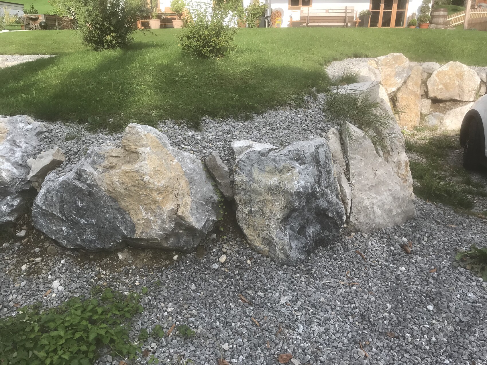 Große graue und beigefarbene Steinblöcke bilden eine Randbegrenzung im Kies- und Grasgarten.