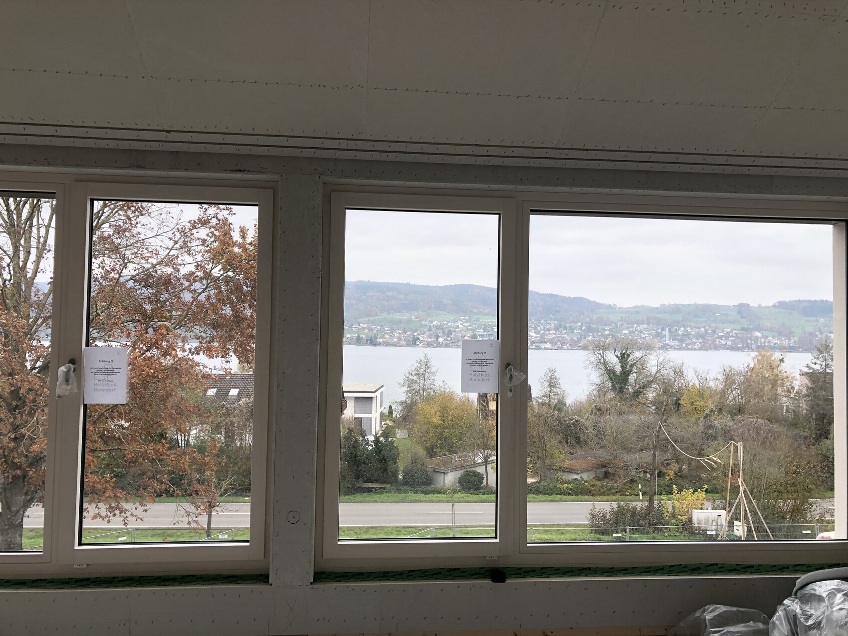 Innenraum mit drei großen Fenstern; Blick auf See, Hügel und Herbstbäume außen