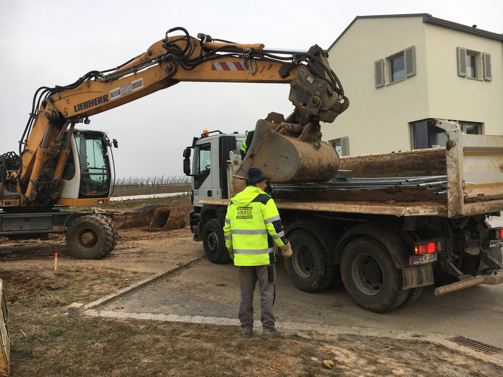 Bauarbeiter in Neon-Weste an Baustelle neben großem Bagger und Kipplader vor Wohnhaus
