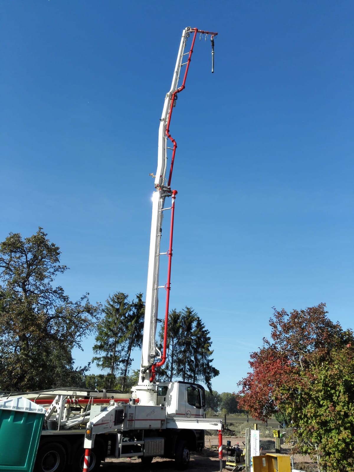 Großer Baukran auf Baustelle mit Betonpumpe und blauem Himmel