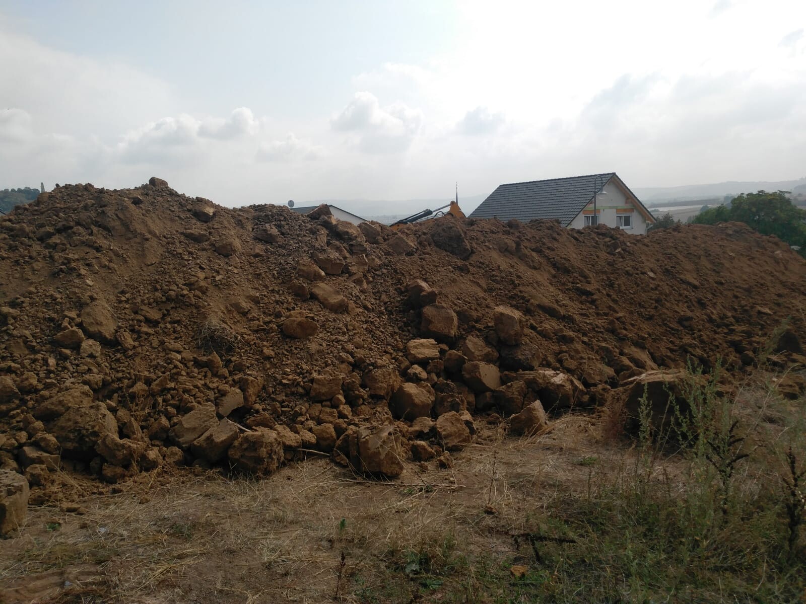 Grosser Erdhaufen vor Baugrundstueck mit Hausern im Hintergrund