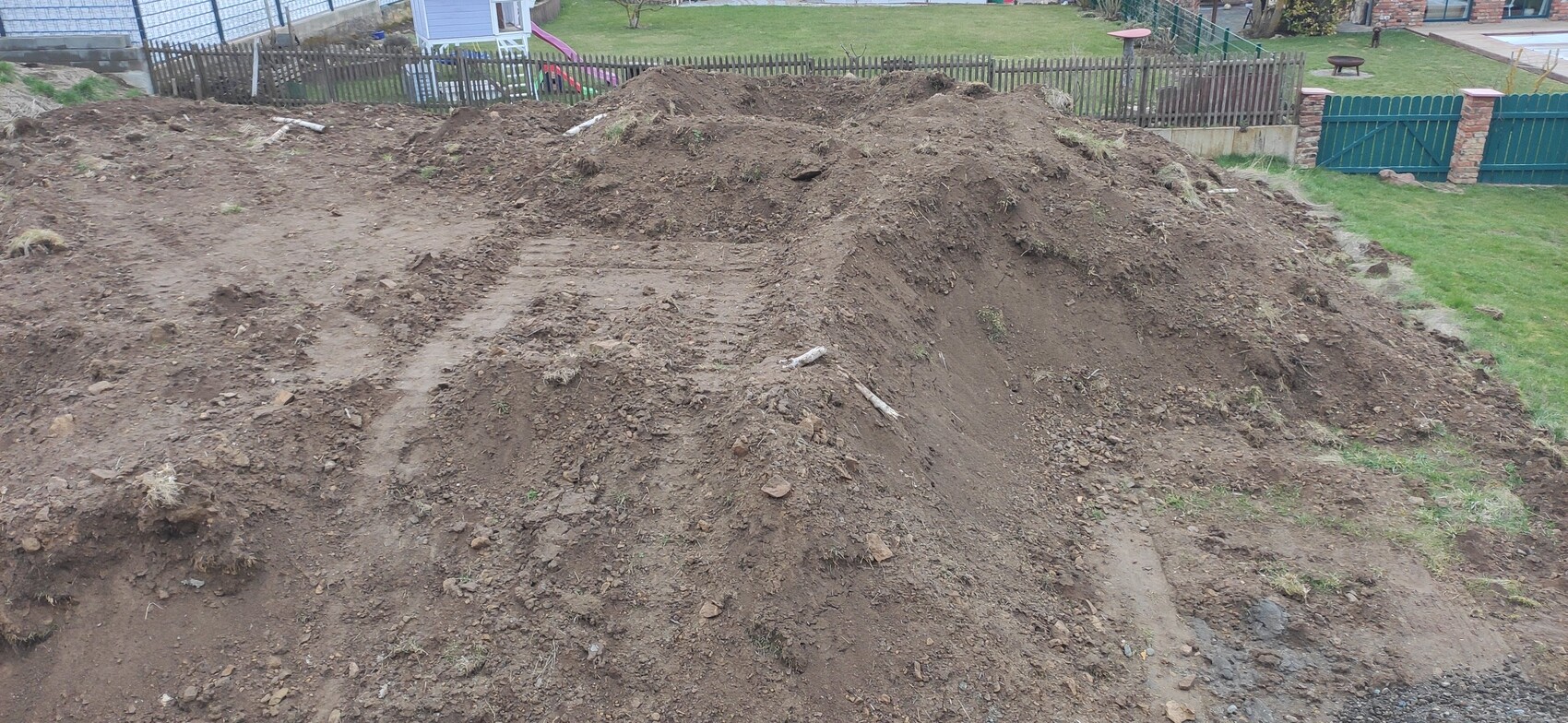 Großer Erdhügel im Garten, lose Erde und Spuren, Zaun und Spielplatz im Hintergrund