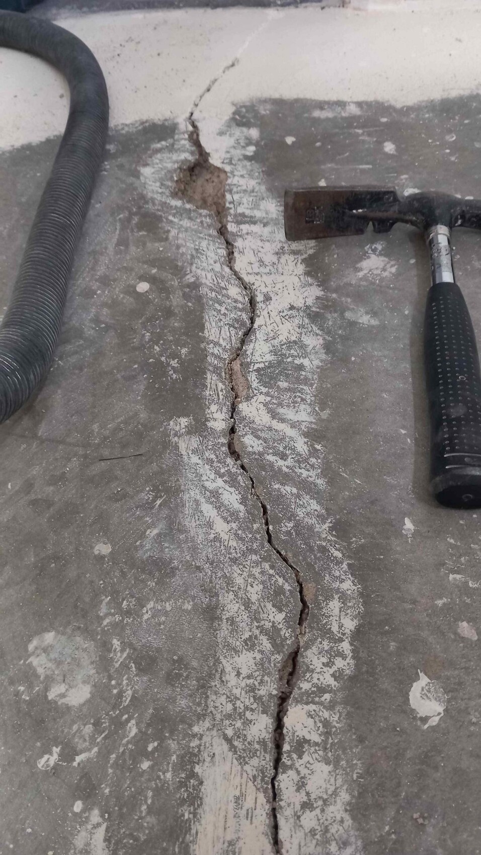 Breiter Riss in einer Betonbodenplatte, daneben Schlauch und Hammer liegen.