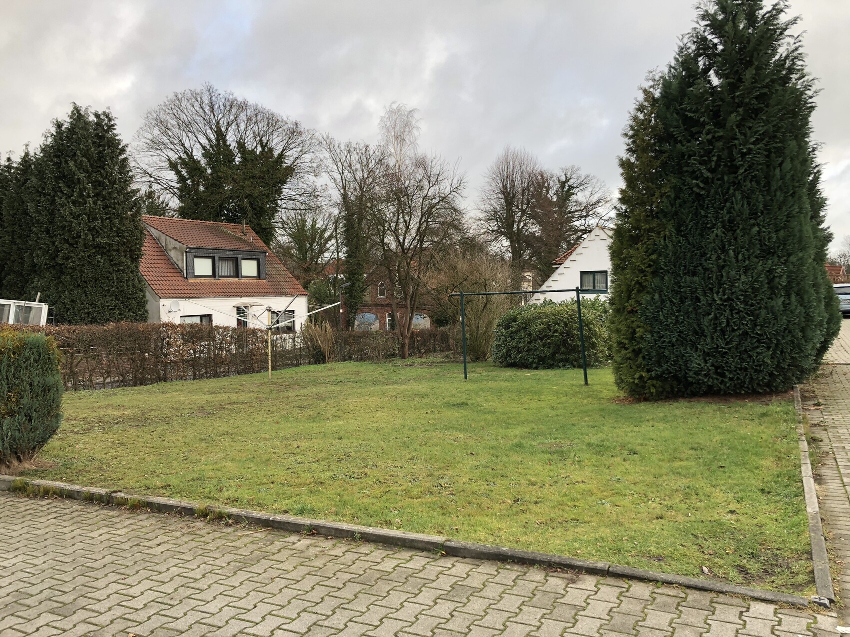 Gartenflaeche mit Gras, Baeumen, Koniferen und angrenzenden Hausern